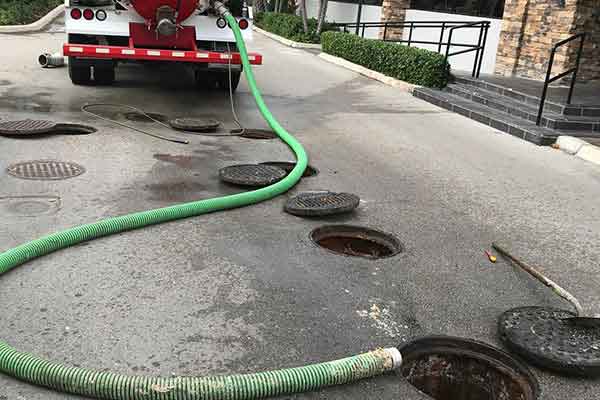 truck cleaning multiple sewer manholes using a large green hose