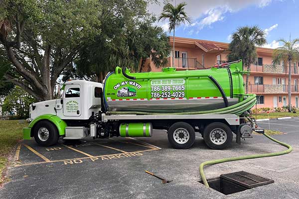 A green septic truck cleaning manhole using hose